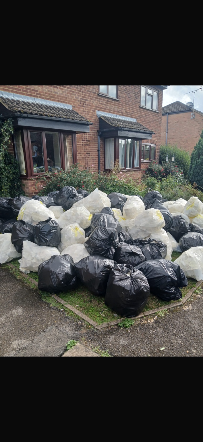 A large collection of black and white waste bags in a front garden before removal.